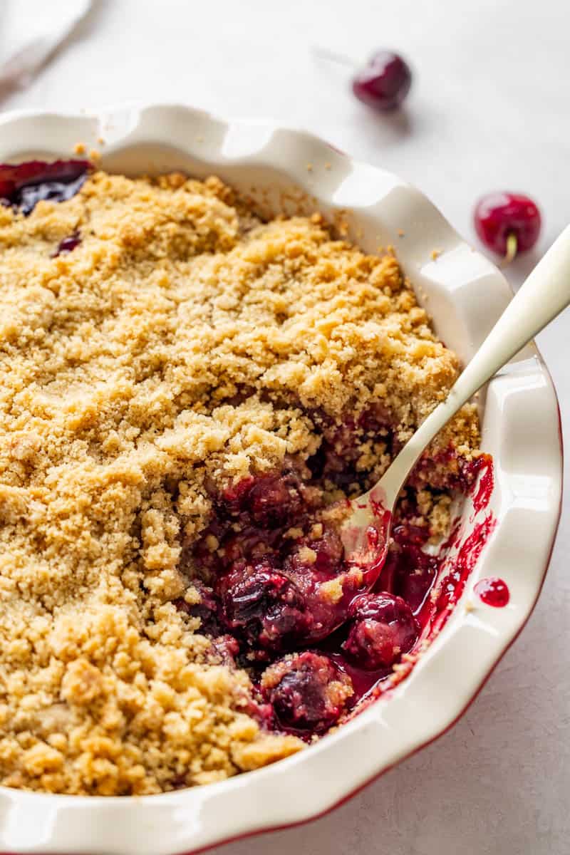 Cherry crumble in a round pie plate with a serving spoon resting in.