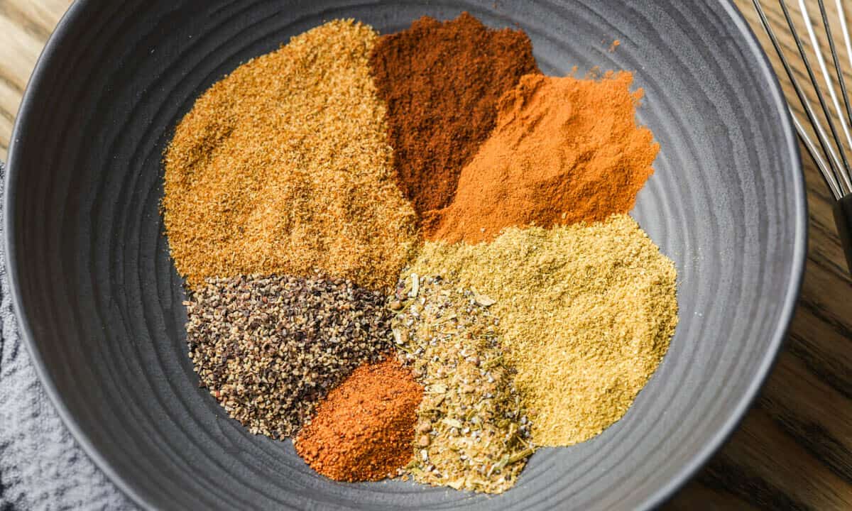 Overhead view, looking into a small black bowl with the individual spices needed to make Garam Masala separated from each other.