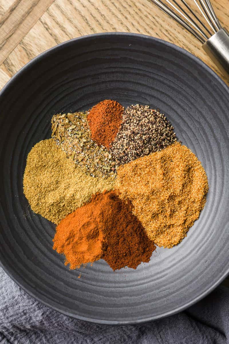 Top view of individual spices to make Garam Masala, in a black bowl.