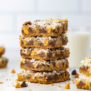 A stack of 7 layer bars on a kitchen counter with a glass of milk in the background.