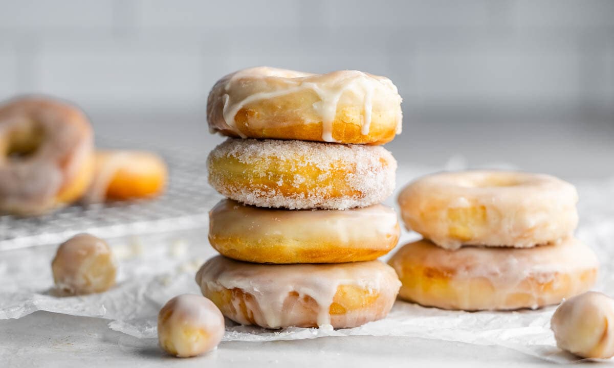 A stack of glazed donuts on a kitchen counter, with donut holes nearby.