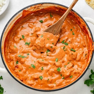 Overhead view of homemade chicken tikka masala in a white large pot with a wooden spoon resting inside.