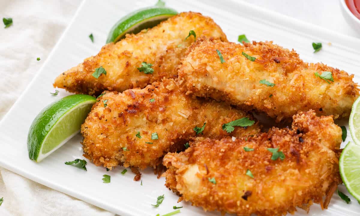 Close up view of coconut chicken tenders on a white serving platter.