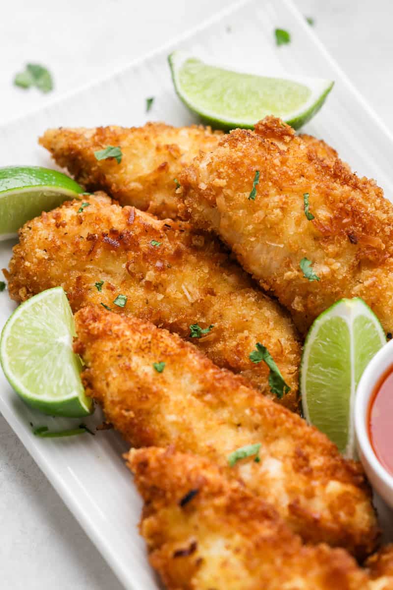 Close up view of crispy coconut chicken tenders on a serving plate.