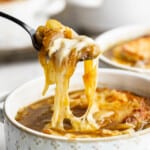 A spoon holding up a bite of French onion soup with melted cheese.