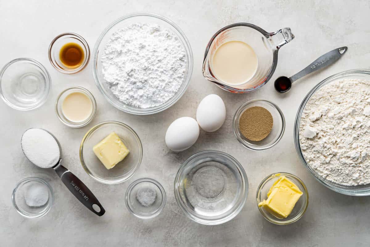Overhead view of a clean countertop with measured out flour, sugar, eggs, butter, vanilla, and other ingredients.
