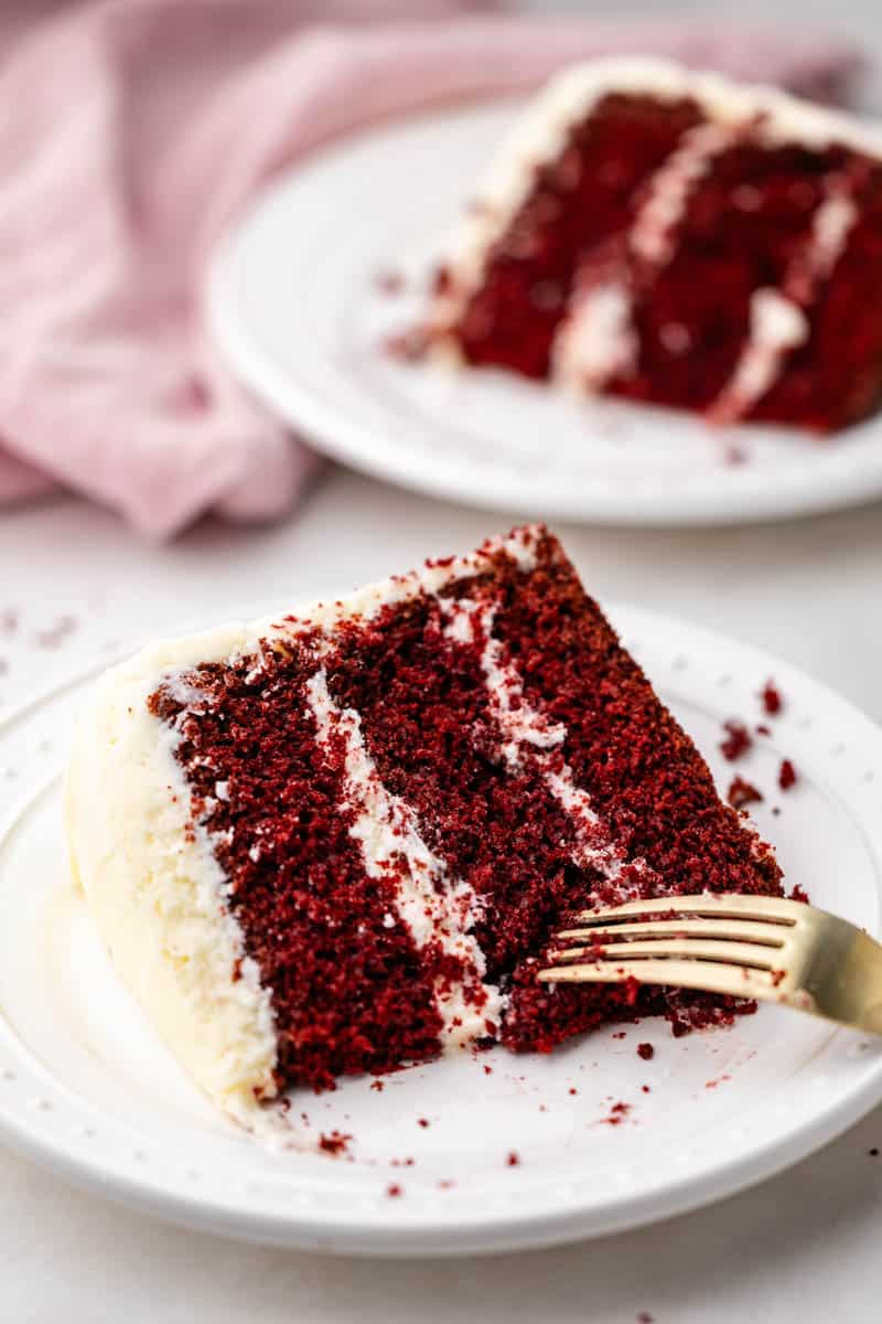 A slice of red velvet cake on a white plate with a gold fork.