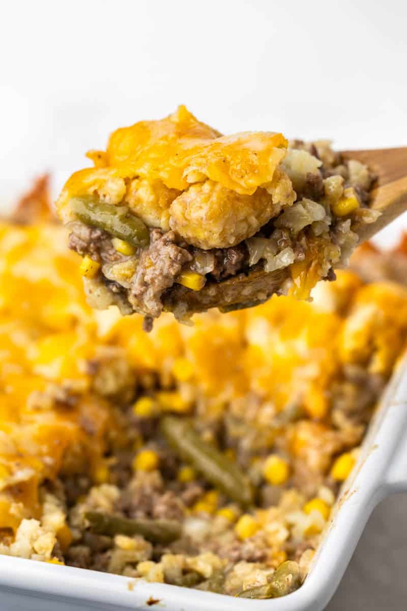 A wooden spoon scooping a helping of tater tot casserole.