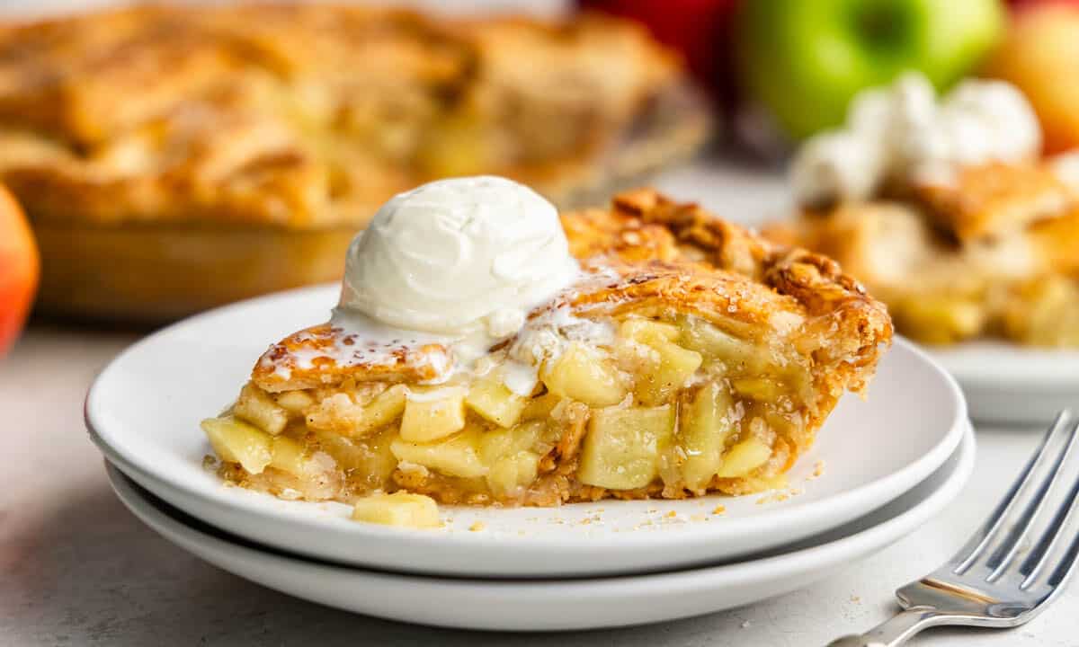 A slice of apple pie on a white plate with a scoop of ice cream on top.