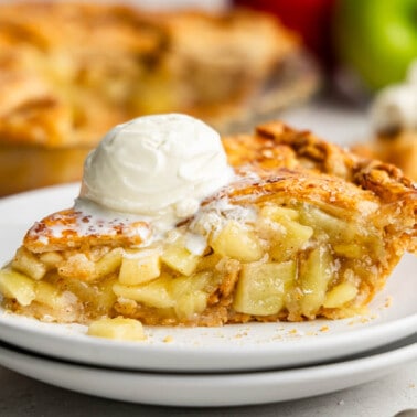 A slice of apple pie on a white plate with a scoop of ice cream on top.