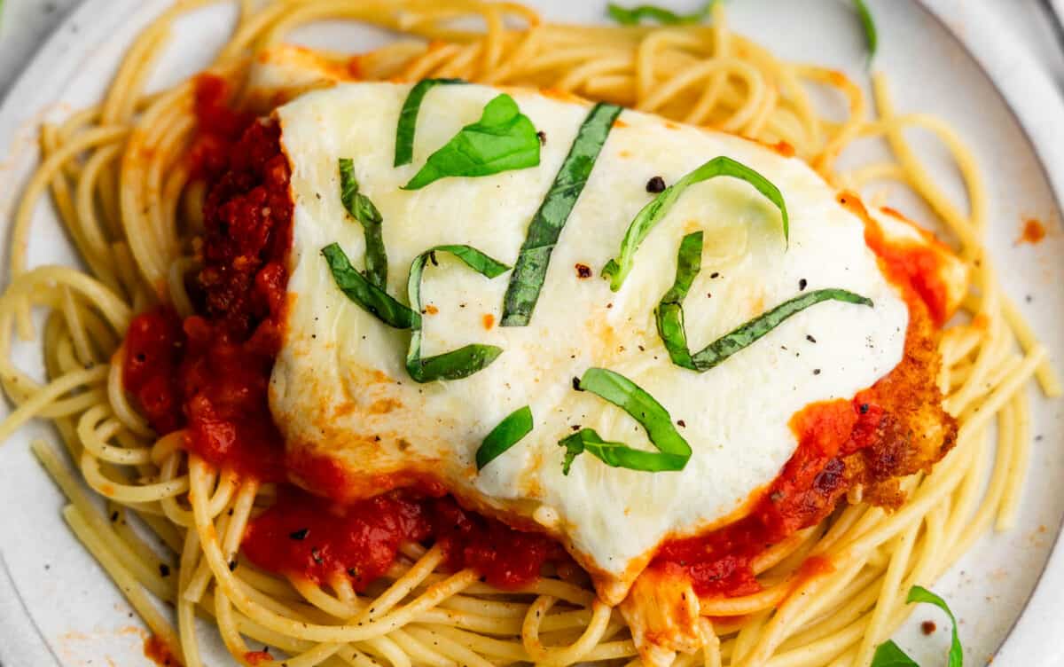 A close up image of a plate of baked chicken parmesan served over plain spaghetti.