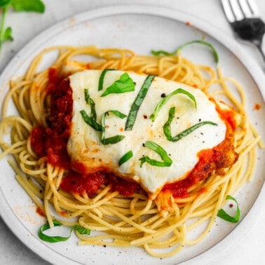 A close up image of a plate of baked chicken parmesan served over plain spaghetti.