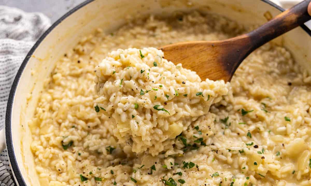 A close up view of a wooden spoon dishing out creamy risotto.