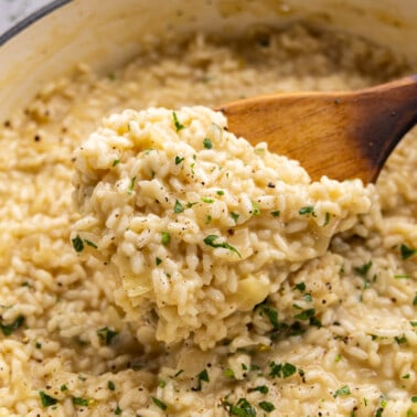 A close up view of a wooden spoon dishing out creamy risotto.