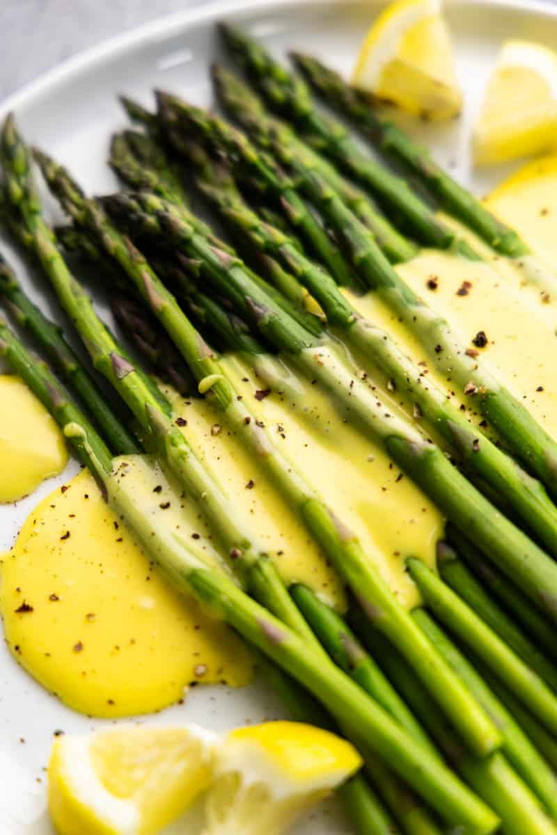 Close up view of hollandaise sauce drizzled on top of asparagus.