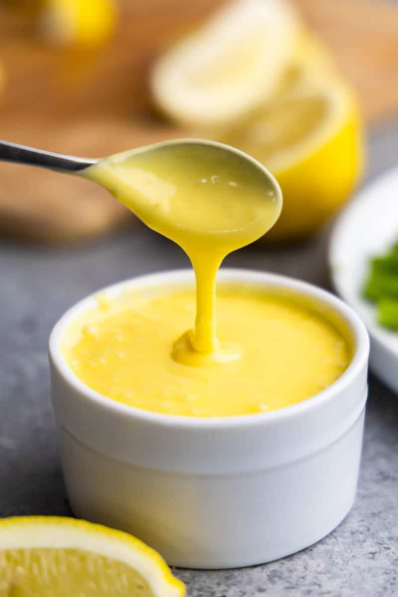 A spoon dripping hollandaise sauce into a small bowl filled with hollandaise sauce.