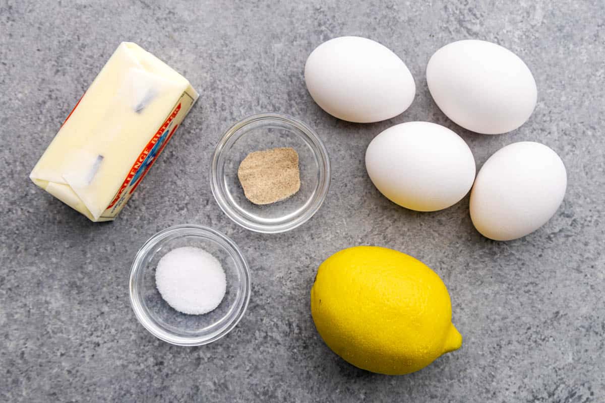 A kitchen counter with eggs, a lemon, butter, salt, and white pepper measured out.