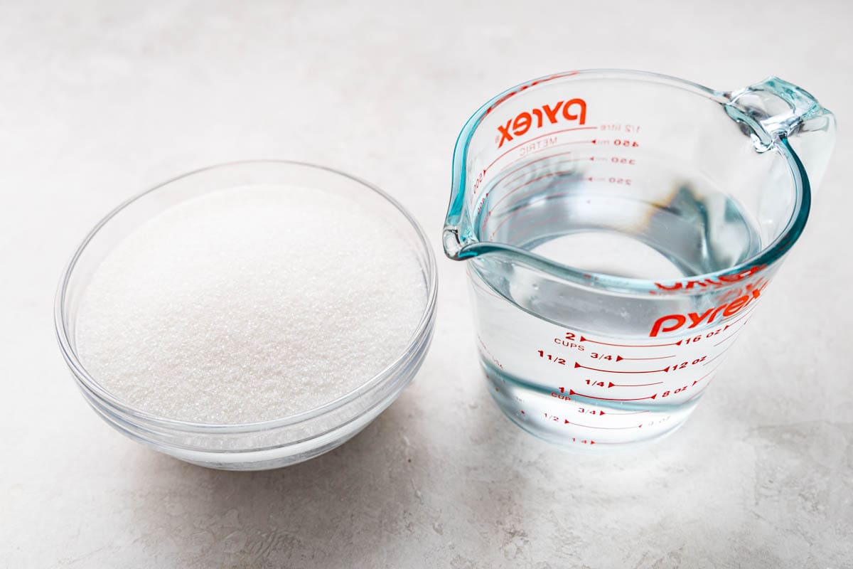 A small bowl filled with sugar and a glass measuring cup filled with 2 cups water.