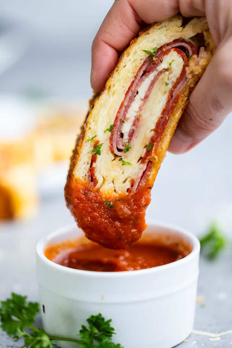 A hand dipping a stromboli into pizza sauce.