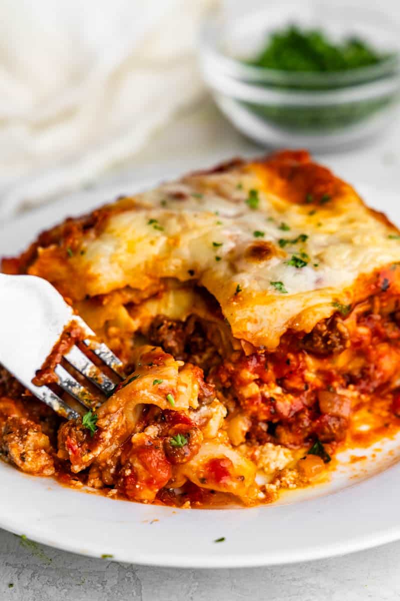 A close up view of a fork cutting a bite out of a piece of homemade lasagna.