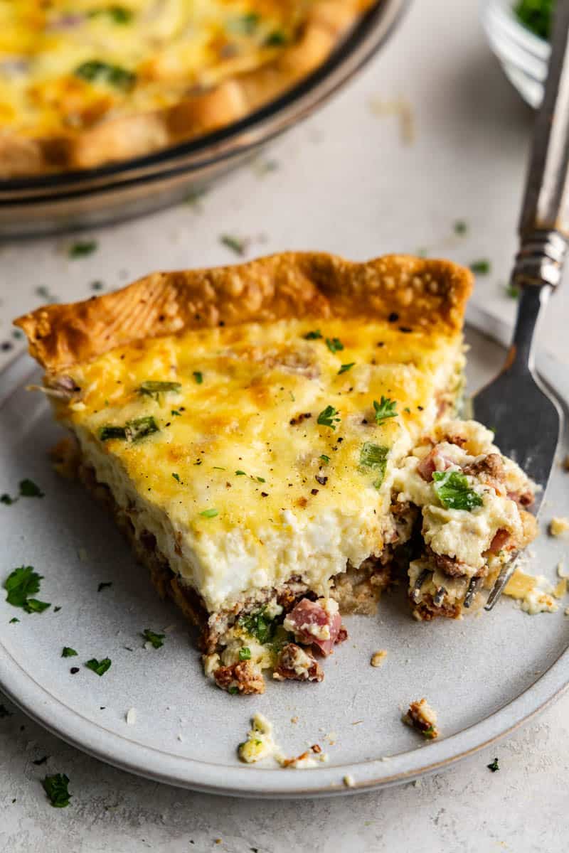 A close up view of a slice of quiche that has been partially eaten, with a fork dishing out another bite.
