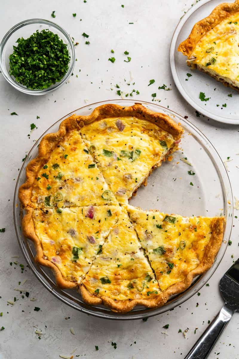 An overhead view of a quiche in a pie plate with a slice missing.