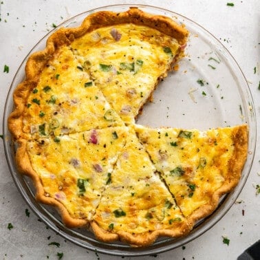 An overhead view of a quiche in a pie plate that is cut and ready to serve with a slice missing.