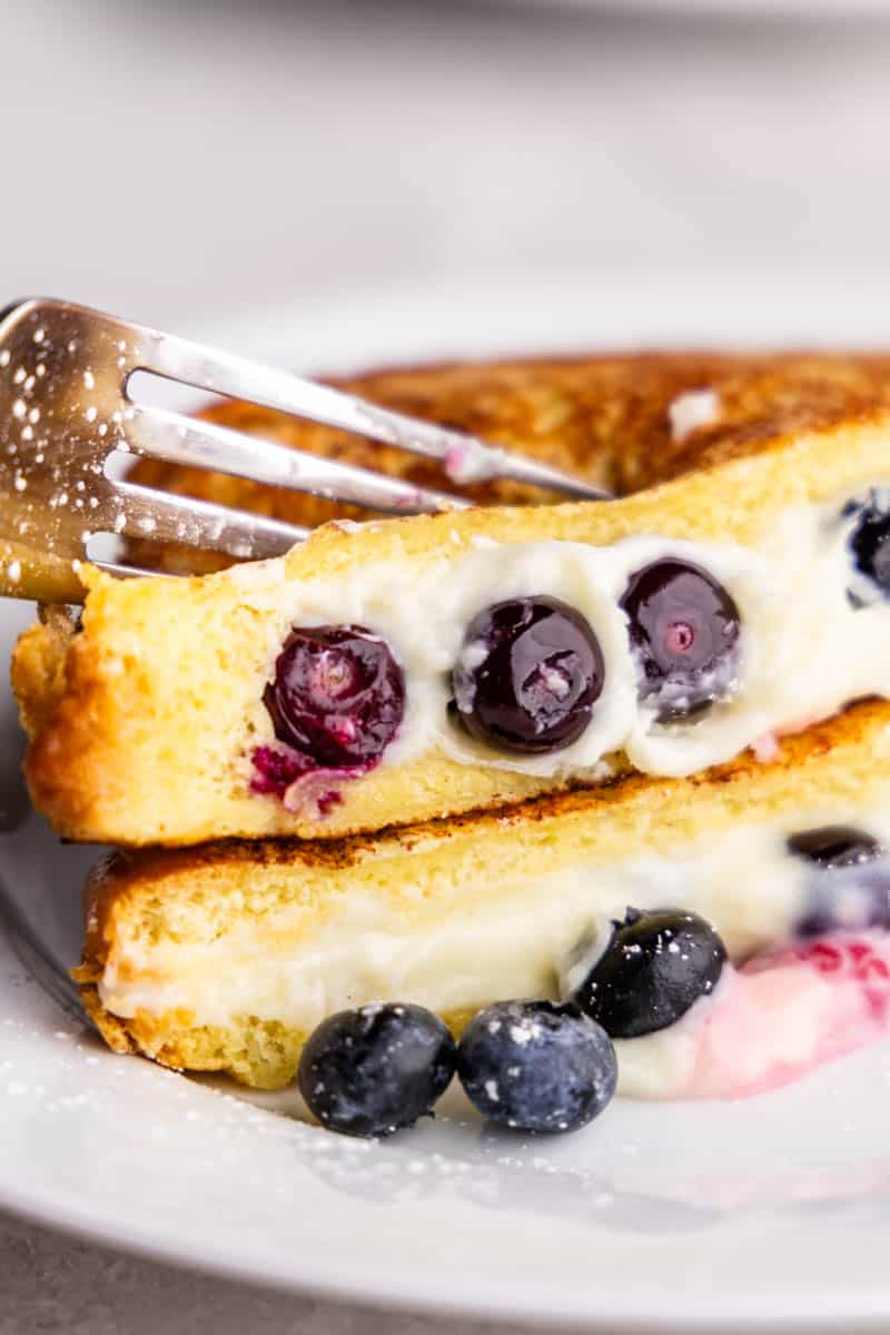 A fork cutting into two stacked pieces of French toast stuffed with cream cheese and blueberries.