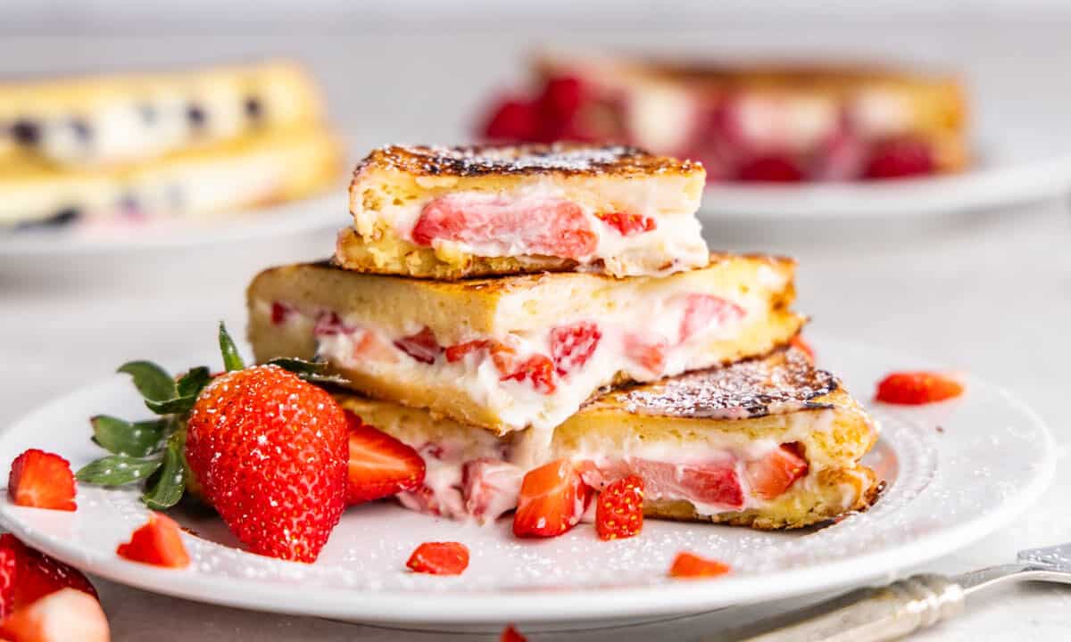 A white plate with French toast stuffed with cream cheese and strawberries.