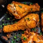 A close up view of 3 pieces of fried chicken being cooked in an air fryer basket.