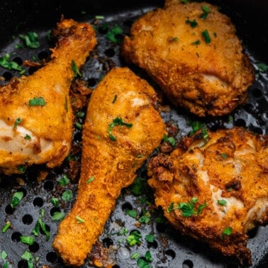 An overhead view into an air fryer basket with four pieces of fried chicken in it.