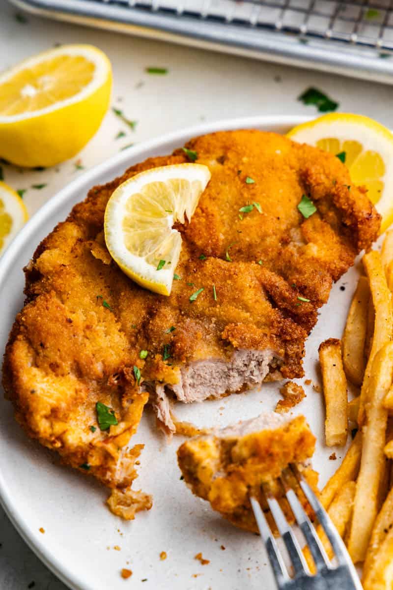 A close up view of schnitzel on a plate that has a bite taken out of it to reveal the pork inside.