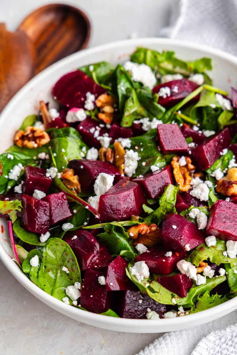 A close up look into a white bowl full of beet salad with nuts and feta cheese.