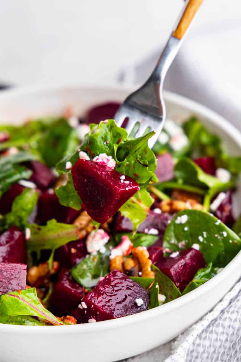 A fork lifting out a bite of beet salad from a bowl.