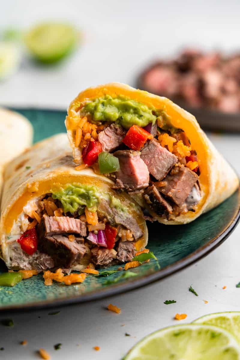 A carne asada burrito on a plate that has been cut in  half so you can see the inside. 
