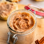A jar of cinnamon butter sitting on a cutting board.