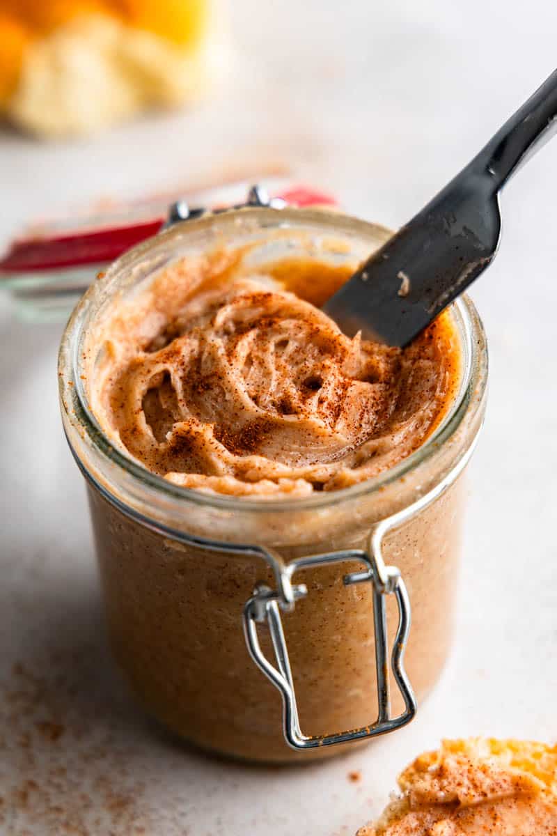 A knife sticking in a small jar of cinnamon butter.