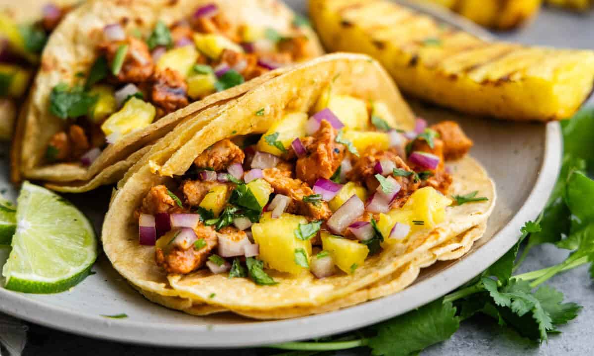 A close up view of an al pastor taco on a plate with grilled pineapple on the side.