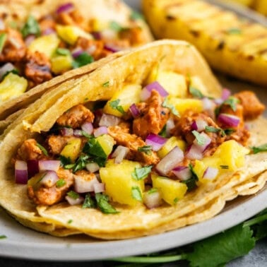 A close up view of an al pastor taco on a plate with grilled pineapple on the side.
