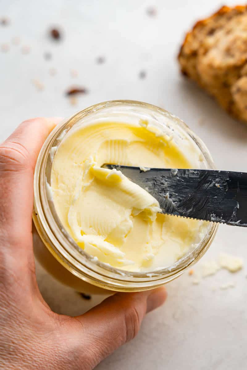 A knife scooping homemade butter out of a mason jar.