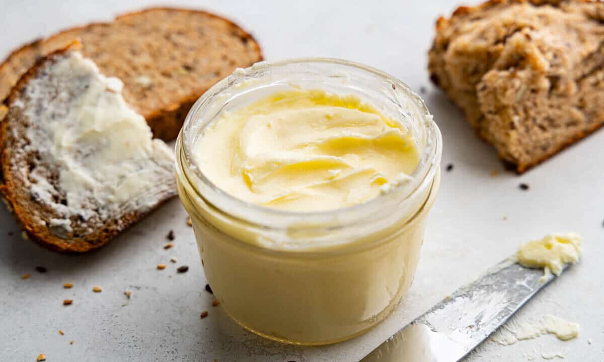 A close up view of a jar of homemade butter with pieces of bread in the background.