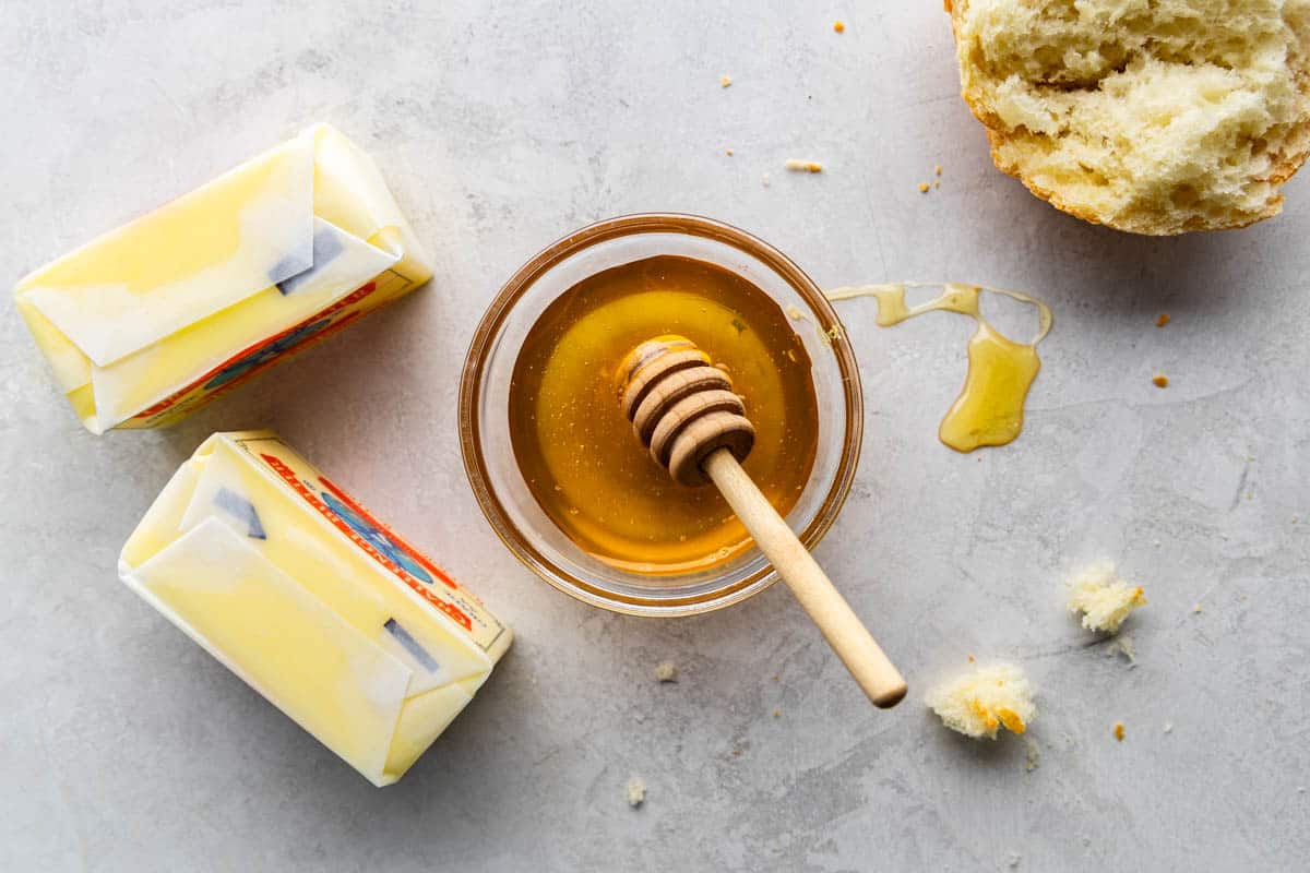 An overhead view of two sticks of butter and a bowl of honey.