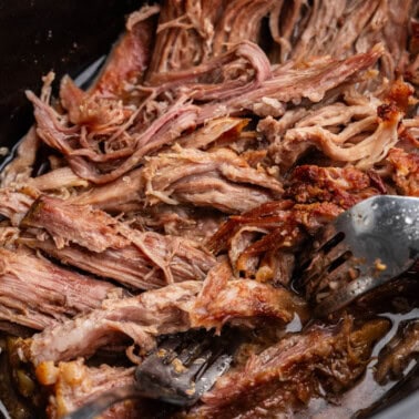 A close up view into a slow cooker with shredded kalua pork.