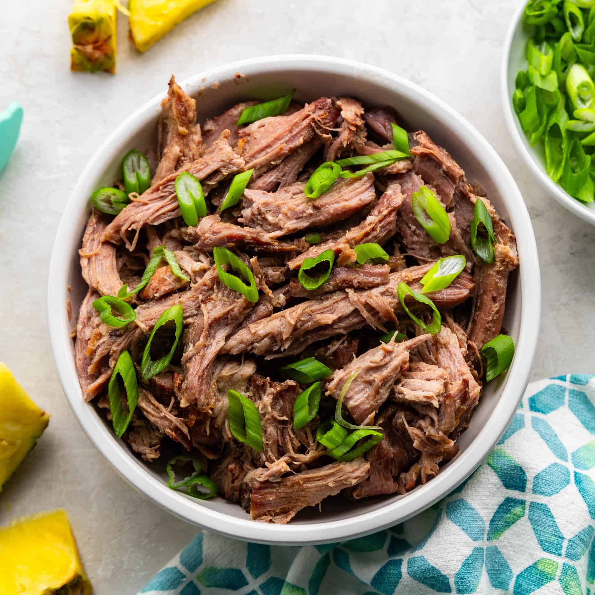 An overhead view of a bowl of shredded kalua pork topped with green onions.