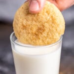 A single snickerdoodle cookie being dipped into a glass of milk.