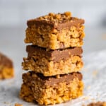 A stack of three toffee scotcharoos on a crinkled piece of parchment paper.