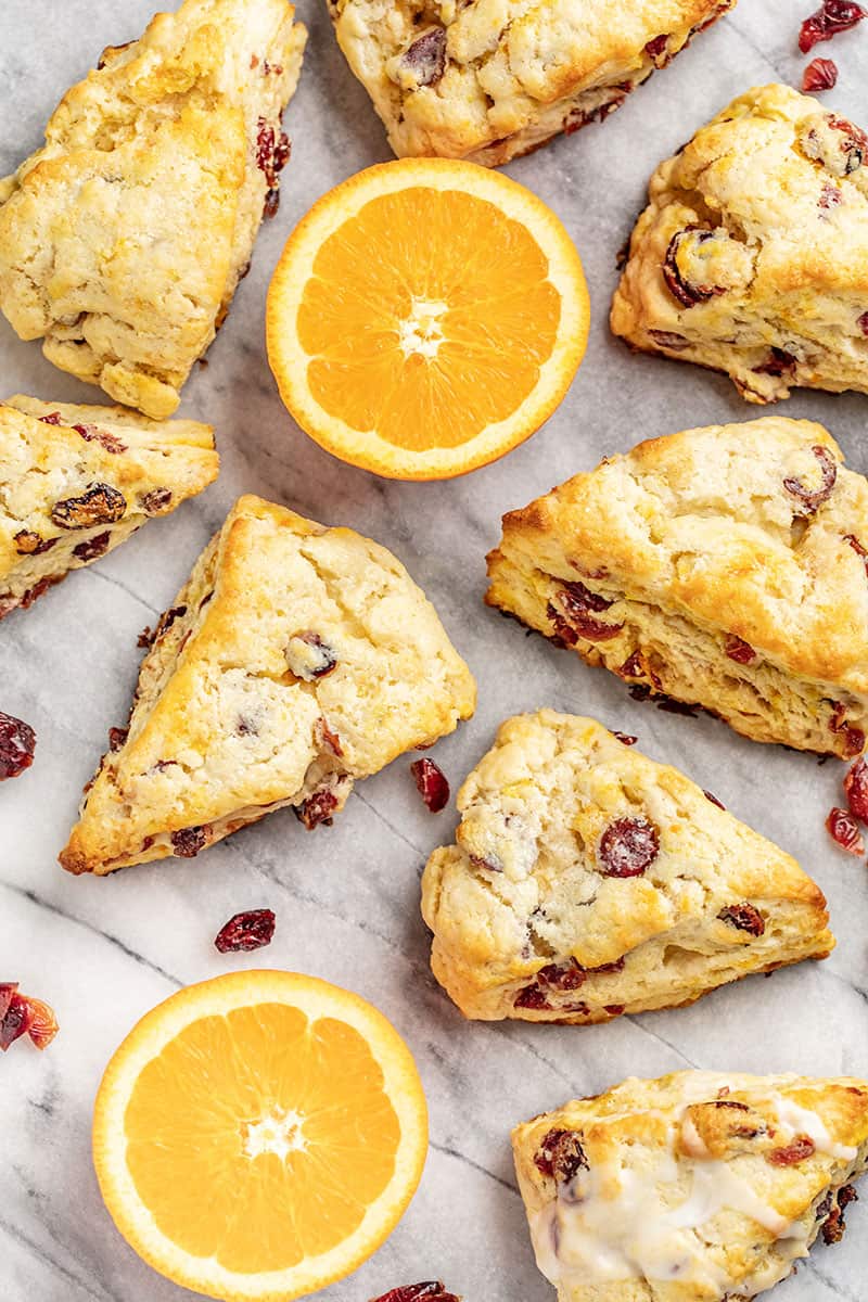 Several cran-orange scones on a table with fresh oranges and cranberries.