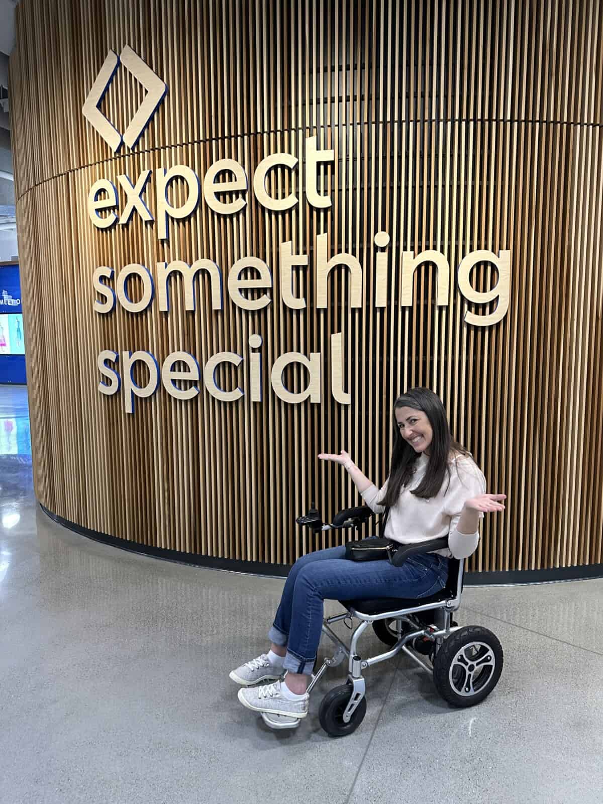 Rachel Farnsworth in a wheelchair at Sam's Club Home Office, in front of their Expect Something Special sign.