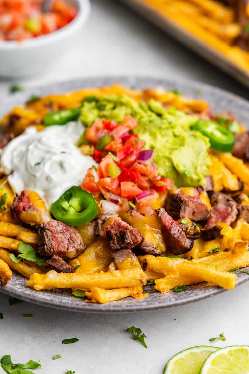 A close up view of a plate of carne asada fries topped with pico, sour cream, and guacamole. 