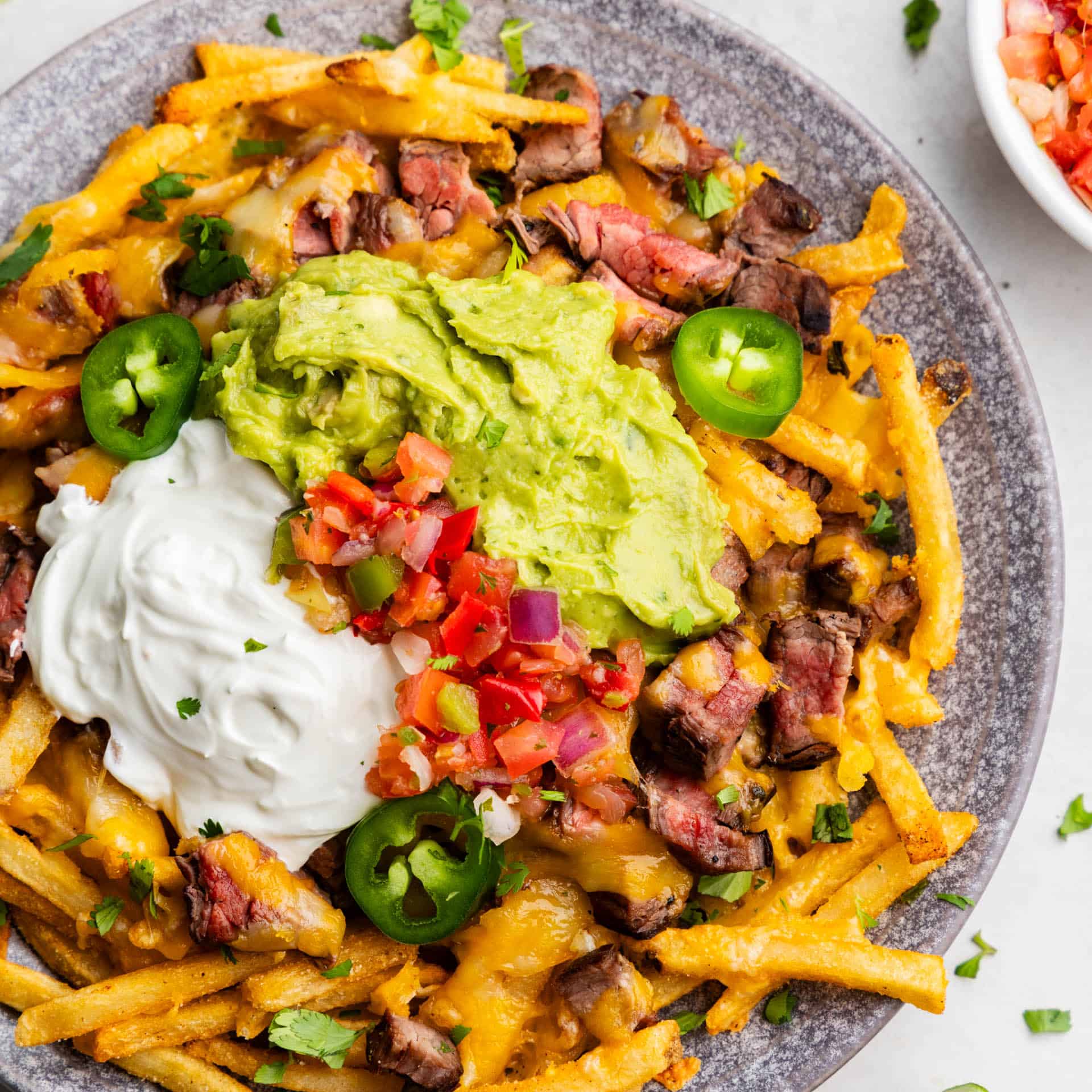 An overhead view of a plate of carne asada fries loaded with pico, guacamole, and sour cream.
